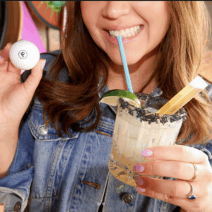 a woman drinking a beverage and holding a golf ball